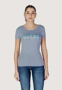 Vaaleansininen lyhythihainen t-paita, jossa on pyöreä pääntie. Mukana "GUESS LOS ANGELES" kiiltävällä sinisellä ja hopealla tekstillä. Pehmeä kangas, istuva malli.