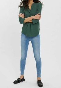 Blouse verte légère avec un décolleté en V et des manches trois-quarts, associée à un jean skinny bleu clair et des mocassins noirs.