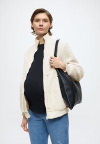 Giacca con zip in pile color crema con polsini a coste, top nero, jeans in denim e borsa in pelle nera morbida e capiente. Texture liscia, design casual.