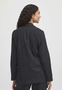 Schwarzes Leinen-Hemd mit langen Ärmeln, lockerer Passform, spitzem Kragen und geknöpften Ärmelabschlüssen, das eine glatte Textur und ein minimalistisches Design zeigt.