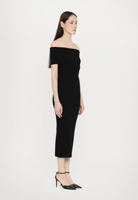 Black off-the-shoulder dress with a fitted silhouette, knee-length. Features a smooth texture and sleek design paired with pointed black heels.