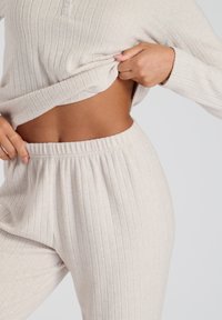 Conjunto de loungewear de punto acanalado en color beige que incluye un top corto y pantalones con cintura elástica, destacando una textura suave y un diseño ajustado.