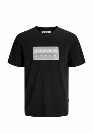 Garçon portant un sweat à capuche gris zippé, un t-shirt noir, un pantalon noir ample et des baskets noires, debout devant un fond clair uni.