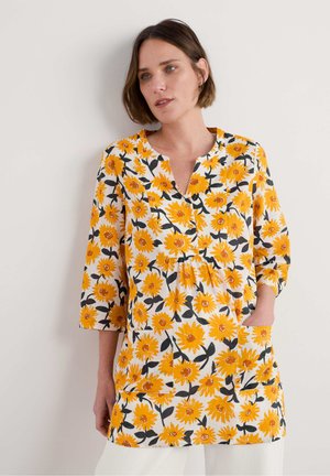 Bloemrijke tuniek top in het wit met felgele zonnebloemen, korte mouwen, een V-hals en een voorzak. Lichtgewicht, zachte stof.