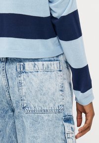 Suéter malha às riscas azul claro e azul marinho combinado com calças cargo de denims claro, apresentando um grande bolso traseiro e um acabamento texturizado.