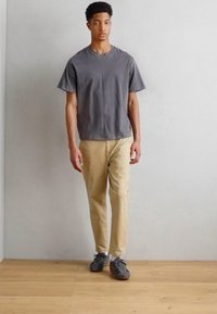 Gray short-sleeve T-shirt made of cotton, paired with beige pants and gray athletic shoes. Simple design, relaxed fit, casual look.
