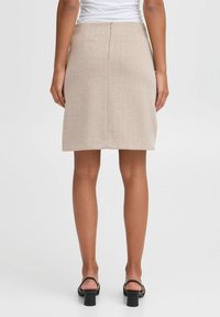 Jupe crayon beige en tissu texturé avec un motif en chevrons, dotée d'une fermeture éclair au dos et d'une silhouette ajustée au-dessus des genoux.