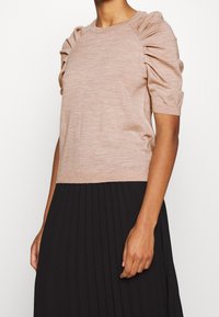 Lichtroze gebreide top met pofmouwen en een geribbelde halslijn, gecombineerd met een zwarte geplooide rok. Soepele textuur en een aansluitend ontwerp.