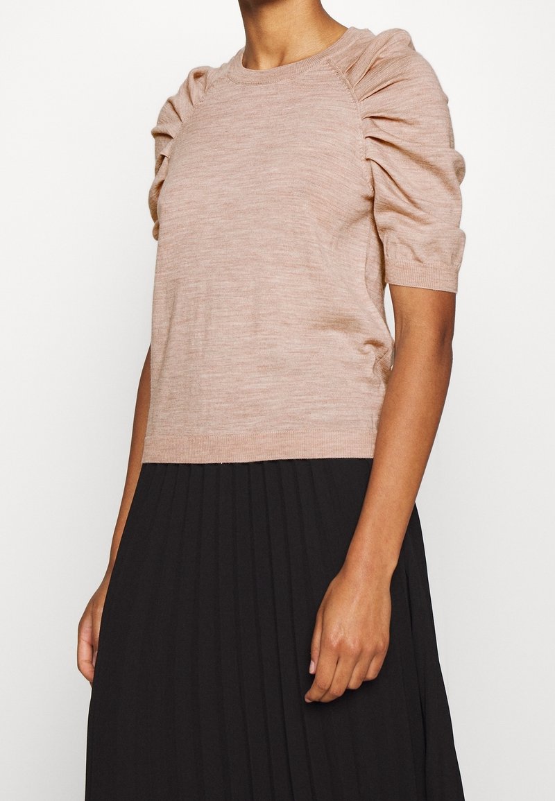 Lichtroze gebreide top met pofmouwen en een geribbelde halslijn, gecombineerd met een zwarte geplooide rok. Soepele textuur en een aansluitend ontwerp.
