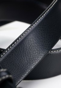 Schwarzer Ledergürtel mit glatter Textur und kontrastierenden weißen Nähten entlang der Kante, der ein langlebiges Design aufweist.