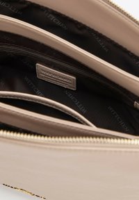 Interno della borsa a mano in pelle beige con più compartimenti, zip dorata e fodera nera con logo. Texture liscia e forma strutturata.