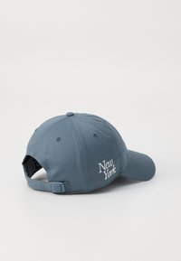 Blå basebollkeps med justerbart band, med broderad text "New York", tillverkad av tyg med en slät yta.