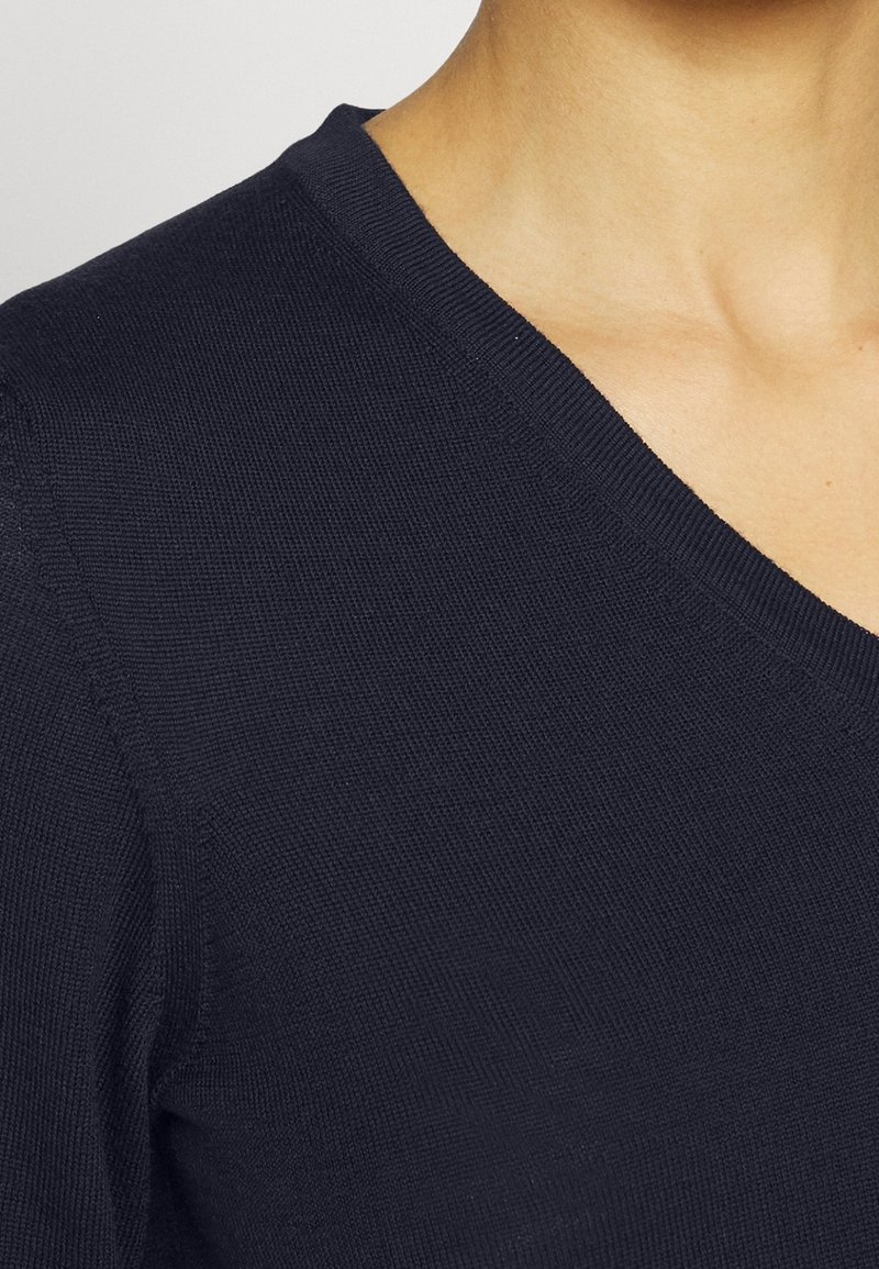 Pull en maille bleu marine avec un design en V, texture lisse et accents côtelés discrets le long du col et des épaules.