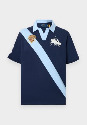 Tumesinine polo-särk helesinise diagonaaltriibu, helesinise krae, valge polo-mängija logoga ja rinnal numbriga tikitud plaastriga.