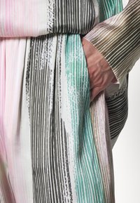 Pruhovaná blůza z měkké tkaniny s vertikálními pruhy v růžové, zelené, hnědé a bílé barvě. Texturovaný detail s uvolněným střihem a kapsami.