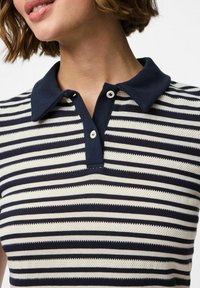 Randig polo skjorta med marinblå krage och knappslå. Tyget har horisontella ränder i marinblått och krämfärg med texturerad stickning.