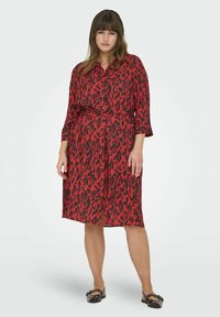 Rode en zwarte luipaardprint shirtjurk met korte mouwen, knopen aan de voorkant, een ceintuur in de taille en een rok die tot op de knie komt. Glad stof met een lichte glans.