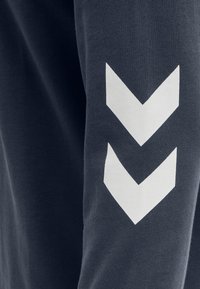 Dunkelblauer Stoff mit zwei weißen, nach unten zeigenden Chevron-Pfeilen, die vertikal gedruckt sind.