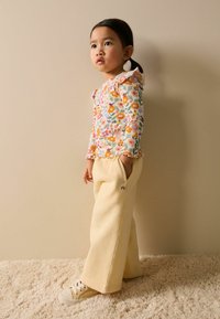 Bluză florală ușoară cu mâneci lungi și guler cu volane, asortată cu pantaloni largi de culoare crem și adidași crem. Material moale, design casual.