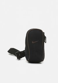 Kompat svart midjeveske med brune kantinger, glidelåslukking, justerbar stropp og Nike-logo foran.