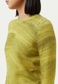 Grön, långärmad tröja med ett strukturerat, virvlande mönster. Har en rund halsringning och slät tyg. Framsidan visar sidoprofil.