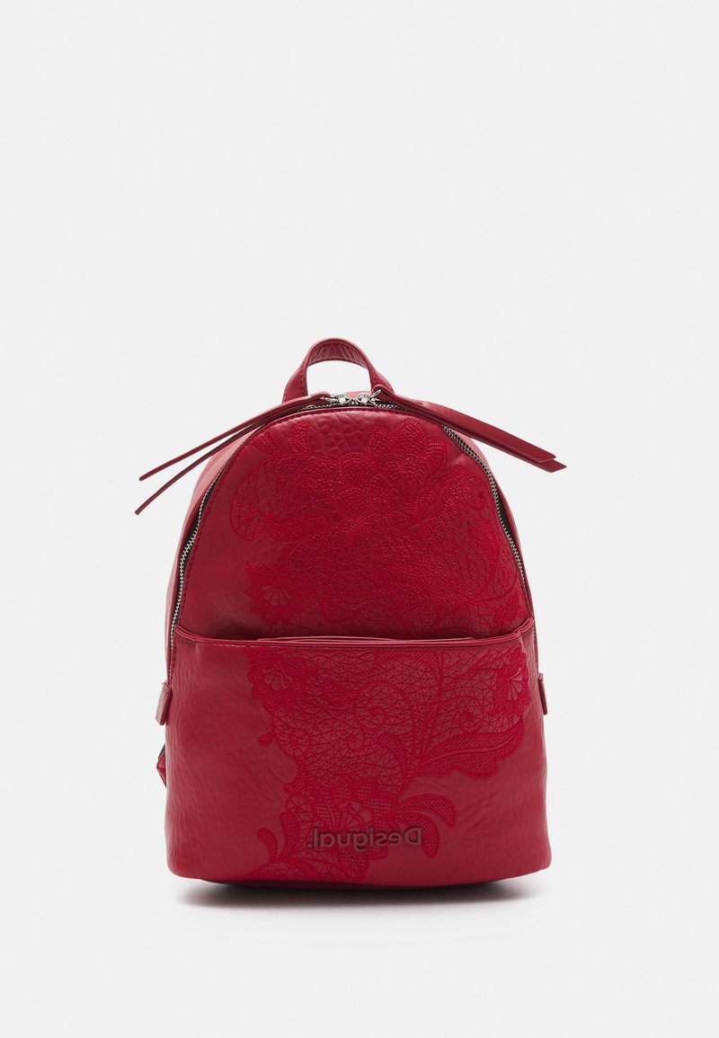 Petit sac à dos rouge avec motif floral embossé et poche avant zippée, debout sur une surface blanche.