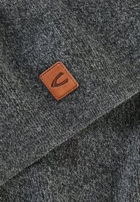 Houtskoolgrijs gebreide stof met een gestructureerde uitstraling, voorzien van een bruine leren vierkante patch met een logo in de hoek.
