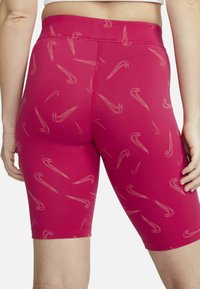 Prigludę rožiniai šortai, pagaminti iš tamprios medžiagos, su subtiliu šviesių „swoosh“ logotipų raštu. Ilgis iki vidurio šlaunies su elastinga juosmens juosta.