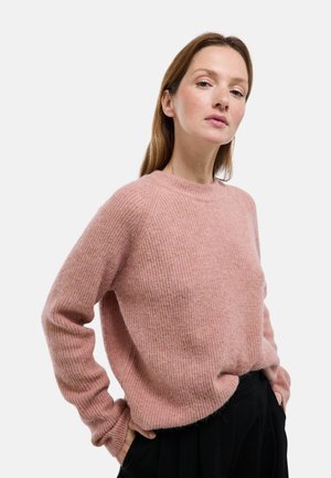 Pull rose clair en tricot avec une texture côtelée, col rond et manches longues, porté par-dessus un pantalon noir.
