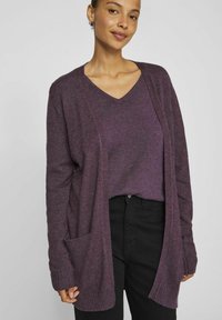 Lila stickad cardigan med v-ringning, öppen framdesign, långa ärmar och en fackficka. Texturerad tyg med mjukt avslut.
