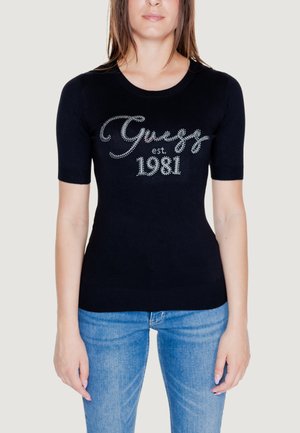 Top corto a maniche corte in tessuto a maglia, con lettering in strass argento "Guess est. 1981" sulla parte frontale. Abbinato a jeans blu.