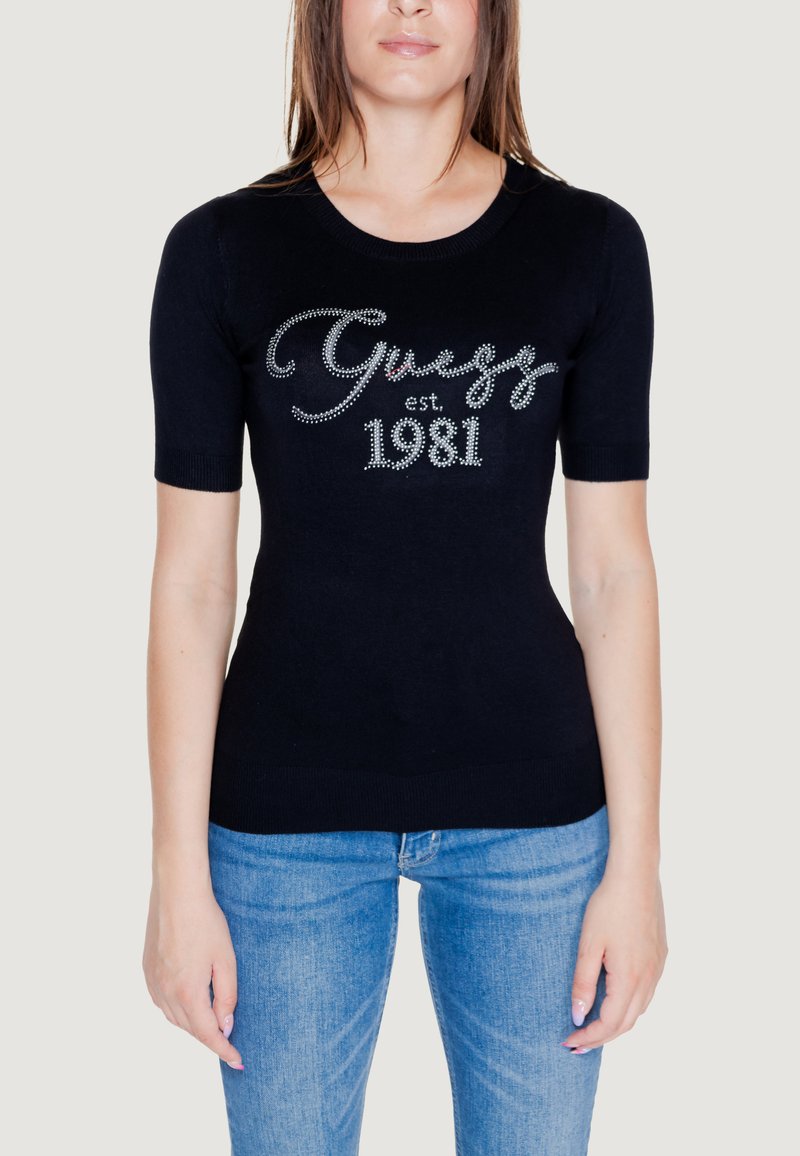 Top corto a maniche corte in tessuto a maglia, con lettering in strass argento "Guess est. 1981" sulla parte frontale. Abbinato a jeans blu.