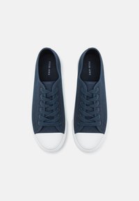 Baskets en toile navy avec semelle en caoutchouc blanche, bout rond, lacets plats et détails de couture subtils. L'intérieur présente la marque PIER-ONE.
