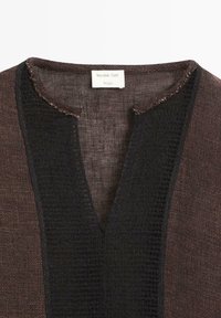 Bruine gebreide top met een diepe V-halslijn voorzien van een brede, getextureerde zwarte rand en een Massimo Dutti Studio-label aan de binnenkant van de kraag.