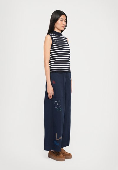 Navy striped sleeveless top paired with loose navy pants featuring colorful text and accents; model wears brown platform shoes.