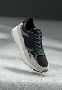 Black and gray sneaker with suede accents, mesh upper, green laces, and a white outsole; notable logo on the heel and streamlined design.