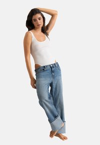 Body blanc côtelé associé à un jean en denim léger bleu clair, ample et retroussé aux chevilles, sur un fond blanc uni.