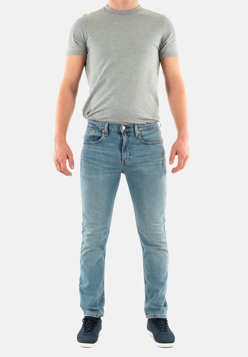 Camiseta gris de manga corta combinada con jeans de mezclilla azul claro. Los jeans tienen un diseño clásico de cinco bolsillos y un ligero desgaste, usados con zapatillas navy.
