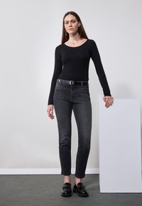 Svart langermet topp kombinert med høyhudet mørkegrå jeans. Merkbart detaljer: subtil falming, belte med sølvtilbehør, og kraftige svarte sko.