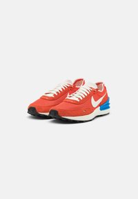 Red mesh sneakers with white laces and a blue midsole. Features suede accents and a black rubber outsole. Notable Nike logo on sides.