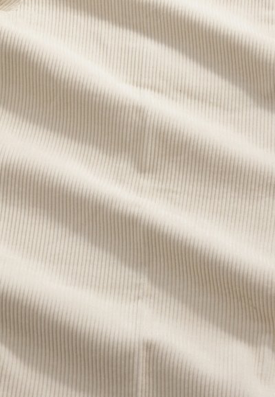 Gestructureerde, roomkleurige stof met een verticaal ribbelpatroon, met zachte, golvende plooien en een subtiele glans.