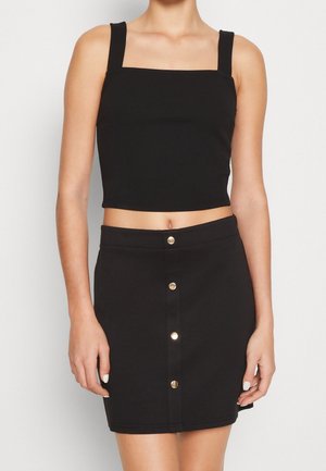 Crop top noir à encolure carrée et bretelles épaisses, associé à une jupe noire avec des boutons sur le devant et une coupe ajustée.