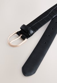 Czarny skórzany pasek z motywem skóry krokodyla i klamrą z metalu w kolorze złotym. Posiada kilka otworów do regulacji rozmiaru. Gładka faktura.