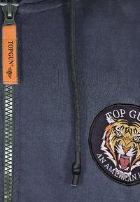 Marine blauwe rits-hoodie met een opvallende tijgerborduursel en "TOP GUN" tekst, zwarte trekkoorden en een leren rits-trekaccent.