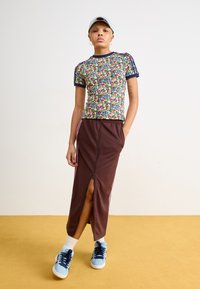 Top de manguitas curtas com padrão floral e acabamentos azul-escuro, combinado com uma saia maxi castanha com fecho éclair frontal e riscas laterais cor-de-rosa. Ténis azul-claro.