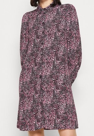 Vrouw draagt een lange-mouw, knoopjessluiting jurk met een roze en zwarte luipaardprint.