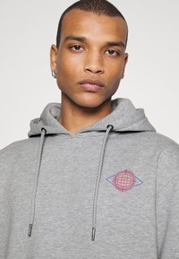Grau Hoodie aus Baumwollmischung mit einem Frontgrafikdesign, das einen Globus in Rot und Blau zeigt. Es hat eine Kapuze mit Kordelzug und metallischen Akzenten.