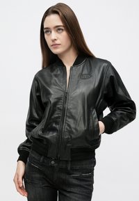 Czarna skórzana kurtka typu bomber z zamkiem z przodu, ściągaczami na mankietach i elastycznym pasem. Posiada logo na piersi oraz boczne kieszenie.