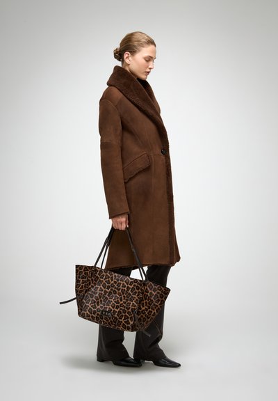 Pruun shearling-mantel suure krae ja esitaskutega, kombineeritud leopardimustrilise käekoti, mustade pükste ja teravate mustade kingadega.