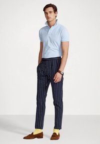 Világoskék galléros pólóklasszikus gallérral, sötét csíkos nadrággal párosítva. Kiegészítők: sárga zokni és barna mokaszin.